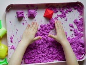ידיים של ילדה נוגעות בחול קינטי בצבע סגול. 