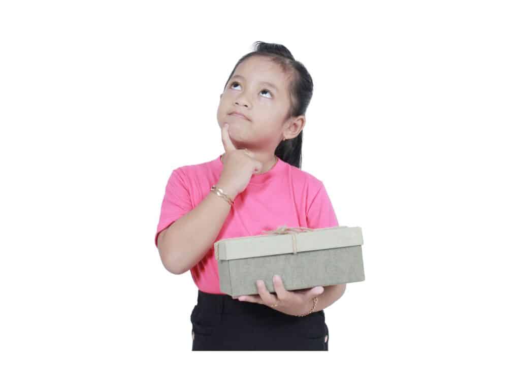 ילדה מחזיקה קופסה וחושבת לעצמה מחשבות, מניחה יד על הסנטר. באתר תוכלו למצוא מגוון מטפלי NLP