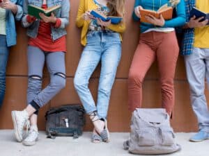 חמישה מתבגרים נשענים על קיר, רואים את פלג גופם התחתון בעודם מחזיקים בידם מחברת קריאה