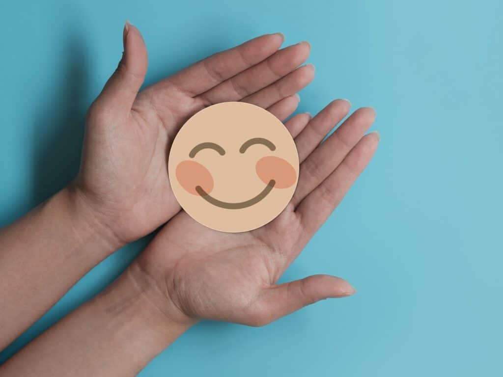 ידיים אוחזות בתמונה של אימוג'י מחייך. באינדקידס ניתן למצוא מגוון של מטפלים בגישה חיובית