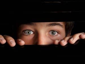 תמונה של ילד מפוחד מציץ מבעד לחלון שחור. ב - INDEKIDS ניתן למצוא מגוון כלים לשיח רגשי בטוח