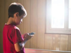 ילד מחזיק טלפון בידו, נראה מרוכז בו. ב - INDEKIDS תמצאו מגוון כלים לשימוש נכון בסמרטפון