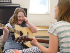 ילדה ומטפלת מנגנות בגיטרה, הילדה מנגבת דמעה. ב - Indekids תמצאו מגוון מטפלים באומנויות.